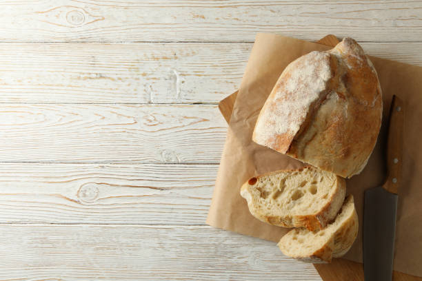 istock Baking paper with bread and knife on white wooden background 1292537219