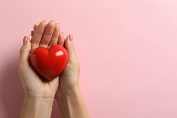 istock Female hands holding heart on pink background, space for text 1292539366