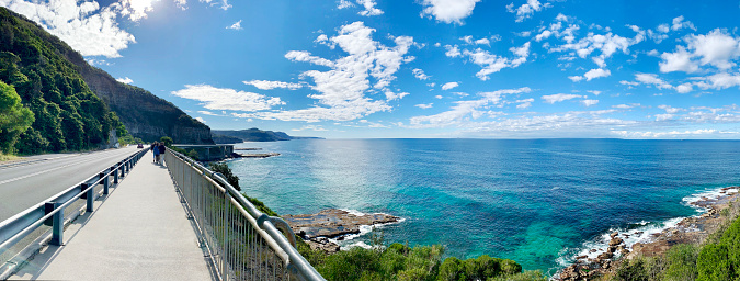 Full HD wallpaper background coastline walkway path along with crystal clear sea, blue sky with white cloud beautiful seascape panorama. High-resolution rock composition of nature coast view.