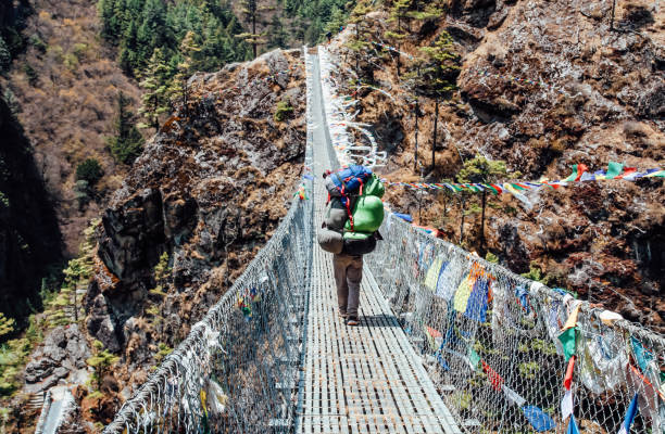 istock Nepal Porter carrying heavy load on his back going along the bridge 1292543093
