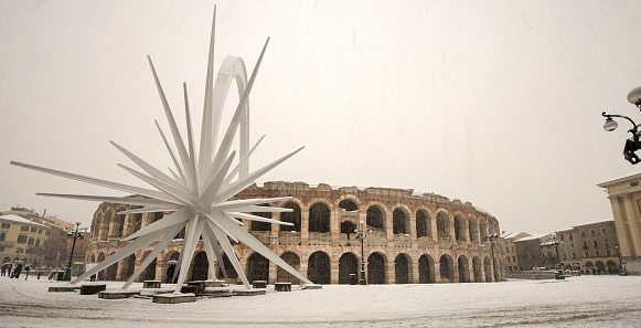 Verona, Italy - Dec 14, 2012: The Arena di Verona in winter with the comet while it snows (I-III century). UNESCO world heritage site. Veneto, Italy, Europe. A group of people strolls in the famous square, Piazza Brà.