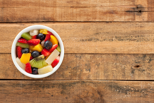 Top view of white bowl full of fruit salad over wooden table
