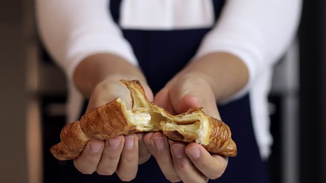 Woman halving a Croissant into two pieces and showing inside