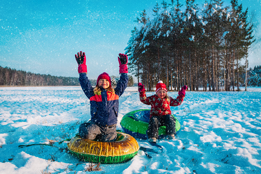 happy little girls slide in winter snow, cute kids have fun outside