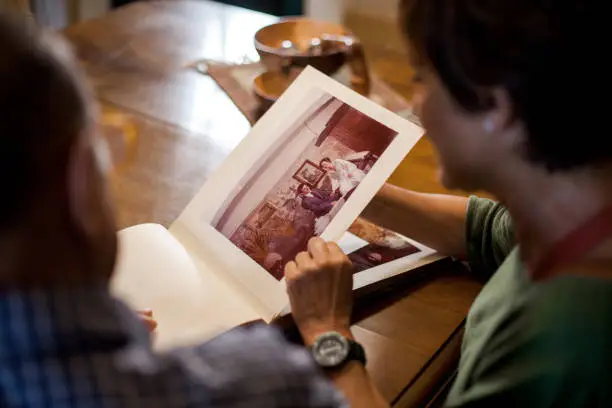 First point of view of a senior man and woman looking at a old wedding photo album. Remembering the past. Mature love. Top shot. Indoor, daytime.