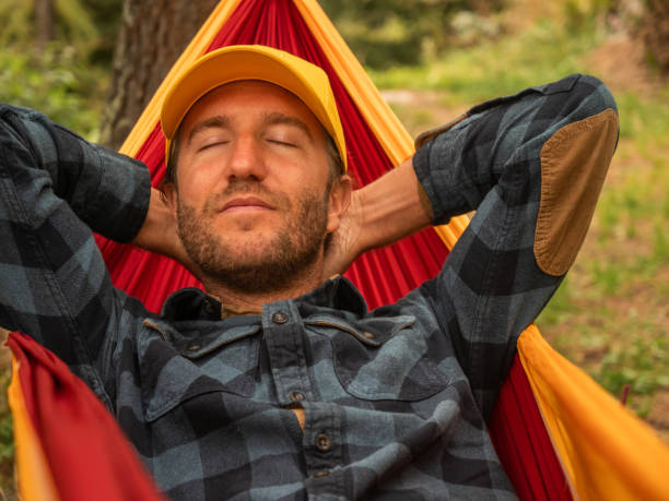 istock Man relaxes in hammock, hands behind head 1292549895