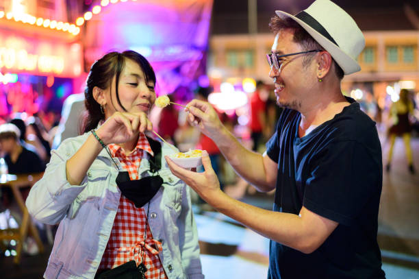 アジアのカップルは、カオサン道路で屋台の食べ物に食べて楽しんでいます - 夜市 ストックフォトと画像
