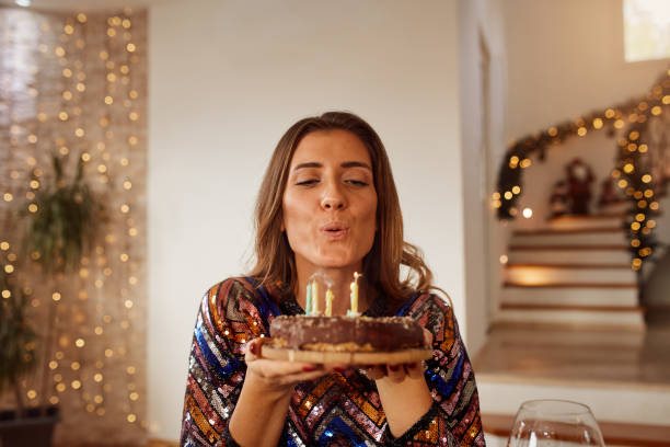 young woman blowing out candles on birthday cake - soprar imagens e fotografias de stock