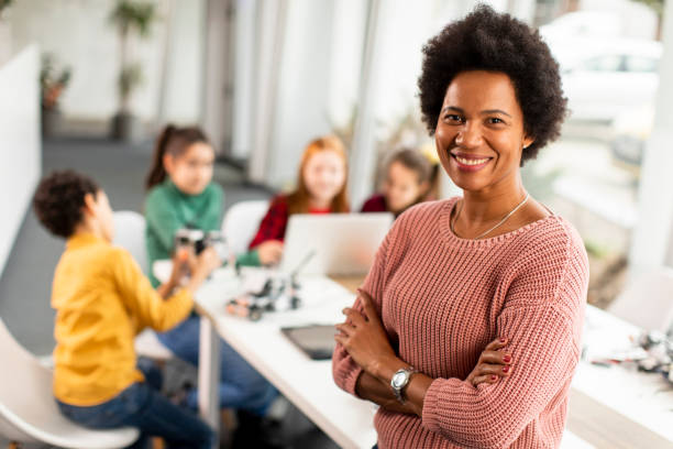 profesora afroamericana de ciencias con un grupo de niños programando juguetes eléctricos y robots en el aula de robótica - teacher fotografías e imágenes de stock