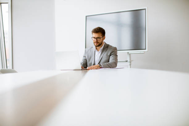 istock Young man working on laptop in bright office with big screen behind him 1292554932