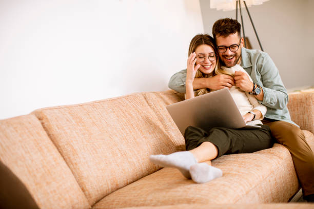 istock Young couple using laptop together while sitting on sofa at home 1292557680