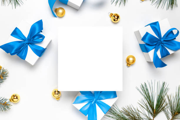 Holiday winter background. White gift box with blue ribbon, New Year balls and Christmas tree in xmas composition on white for greeting card. Flat lay, top view, copy space.
