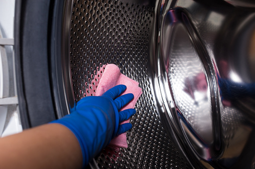 A hand in gloves washes the washing machine with a cloth