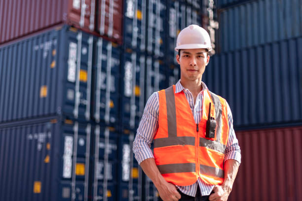 istock Asian logistics control worker professional wear safety helmets and protect suite working in shipping containerin commercial transport background. 1292567975