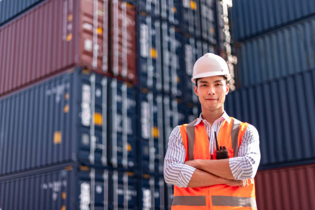 istock Asian logistics control worker professional wear safety helmets and protect suite working in shipping containerin commercial transport background. 1292567980