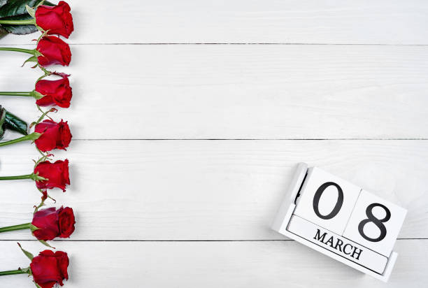 istock Beautiful red roses border with cube calendar on white wooden background, copy space for text. Save the date white block calendar for Womens Day, March 8. Greeting card. Top view, flat lay 1292568249