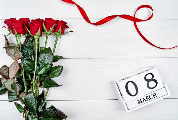 istock Red roses with cube calendar and ribbon on white wooden background, copy space for text. Save the date white block calendar for International Womens Day, March 8. Greeting card. Top view, flat lay 1292568262