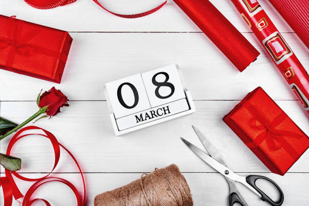 istock Gift wrapping background, copy space. Rolls of red paper, ribbon, gift boxes, rose, scissors and wooden calendar March 8 on wooden background, free space. Flat lay, top view. Greeting card, Womens Day 1292568268