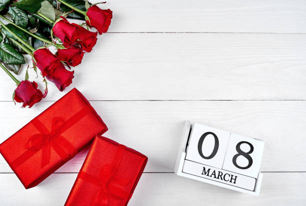 istock Red gift boxes, roses and cube calendar on white wooden background, copy space for text. Save the date white block calendar for Womens Day, March 8. Greeting card. Top view, flat lay 1292568275