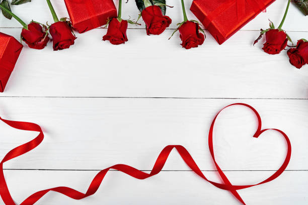 Top view of red roses, gift boxes and ribbon shaped as heart on white wooden background, copy space. Greeting card mockup for Valentines Day, Womans Day, flat lay. Love concept stock photo
