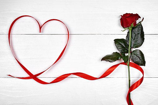 Valentines Day background with one red rose and ribbon shaped as heart, copy space. Greeting card mockup for Valentine Day, Womans Day (March 8), Mothers Day. Love, wedding concept, Top view, flat lay