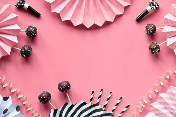 istock Decorative frame with copy-space. Yummy cake pops covered with chocolate and colored sugar icing. Creative monochrome flat lay on pink paper decorated with tasty pop cakes and folded paper fans 1292569240