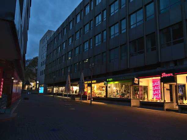 Deserted shopping street in city center with row of closed stores during Covid-19 lockdown and illuminated shop windows in evening in Christmas season. stock photo