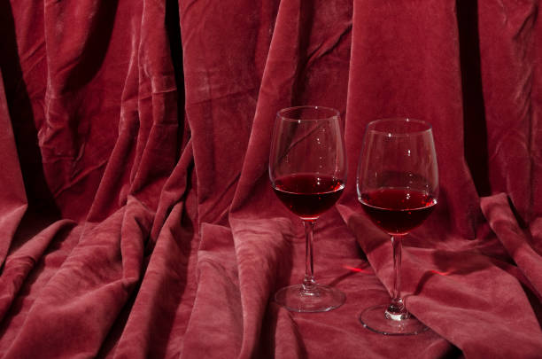 Vertical image.Two glasses and red wine in it, pink decorative textile