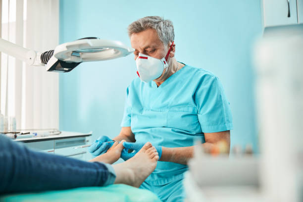 chiropodist podiatrist in blauer uniform und handschuhe mit medizinischem werkzeug in der hand während der behandlung verfahren an den füßen - podiatrist stock-fotos und bilder