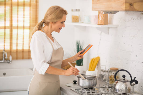 istock Woman in apron cooking and watching something online 1292575804
