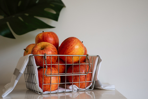 Bunch of gala apples in wire basket on white background with copy space