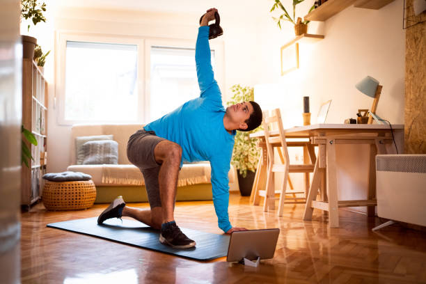 Young man exercising turkish get-up with a kettlebell, online workout on tablet