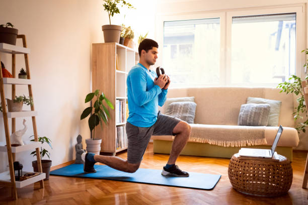 istock Young man working out split squats with kettlebell, online workout on laptop 1292577184
