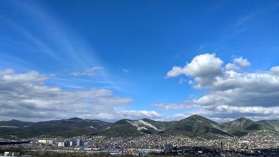 Cumulus clouds floating in the blue sky over a mountain town in spring.