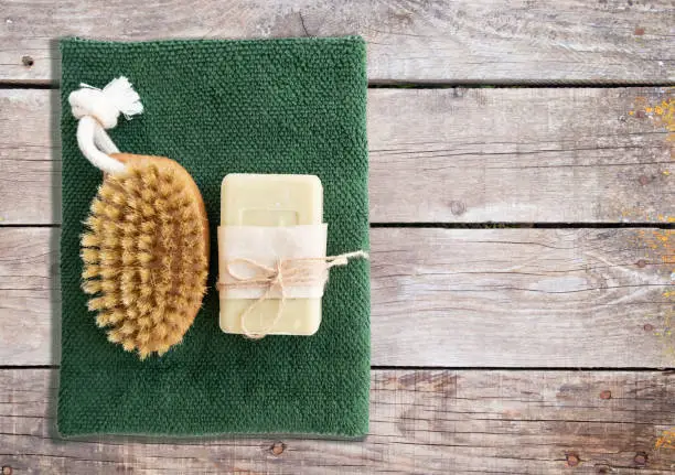 Natural soap and massage brush with a towel on a wooden background with space for text.