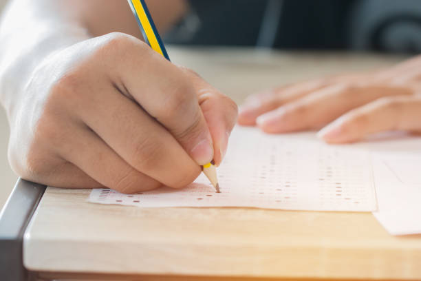istock Education test concept : Man Hands high school, university student holding pencil for testing exams writing answer sheet and exercise for taking in exam paper on wood table at classroom with uniform 1292585274