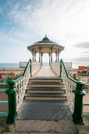 As the sun sets on Brighton Beach, people can be seen in the background. The Brighton Bandstand in the centre is regarded as one of the finest remaining examples of Victorian style bandstands.