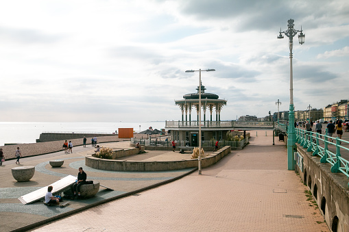 People walking on the promenade and on the street overlooking Brighton Beach with Brighton Bandstand in the background