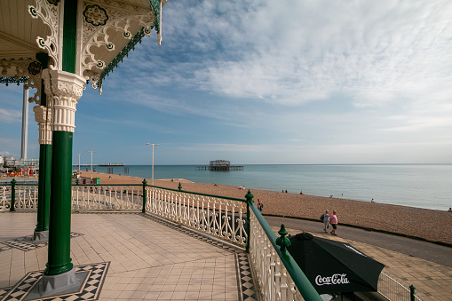 West Pier in Brighton, England, taken from the Brighton bandstand. People can be seen on the beach and a Coca-Cola advert on the patio umbrella