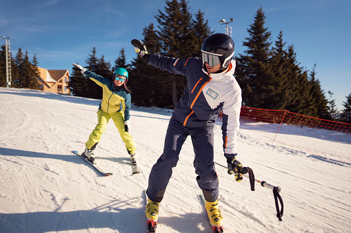 Ski instructor teaching young woman a basics of  skiing at a ski slope on the sunny mountain.
