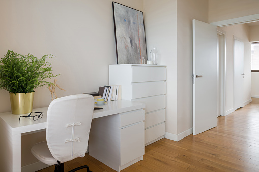 Simple study room with white chest of drawers, white desk and chair and wooden floor
