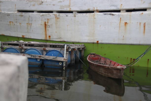 A photo of a small canoe tied to a larger ship with some piece of blue barrel beside it