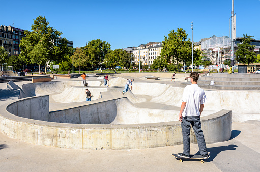 Geneva, Switzerland - September 8, 2020: A dozen young people, boys and girls, are skateboarding at the skatepark of Plainpalais on a sunny afternoon.