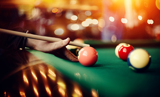 Colorful billiard balls on a green billiard table. Gambling game of Billiards. Hand with a cue.
