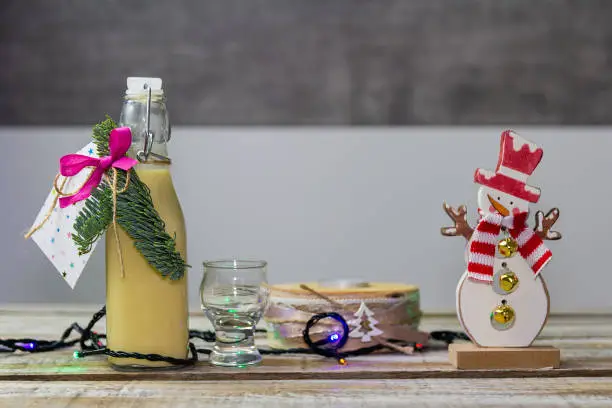 Photo of Homemade alcohol egg liquere with jar, candle and snowman decoration on wood table