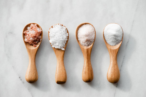 Salt Types Various salt types in 4 wooden spoons on white marble. salt seasoning stock pictures, royalty-free photos & images