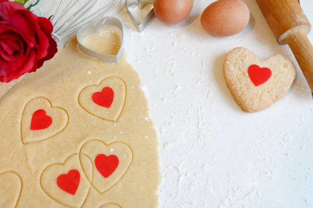 Baking concept for St. Valentines Day with heartshaped cutters and eggs on white wooden table with red flower rose, copy space