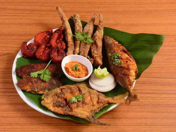 Indian Fish Platter (bangda fish fry,prawns 65,pomfret tawa fry,bombil fry and surmai fry) Popular sea food starter from india  served in a banana leaf over a white ceramic plate, selective focus