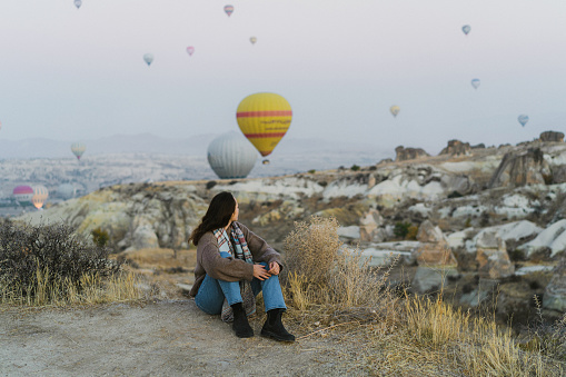 Young Caucasian woman sitting and looking at hot air balloons in  Cappadocia in Turkey