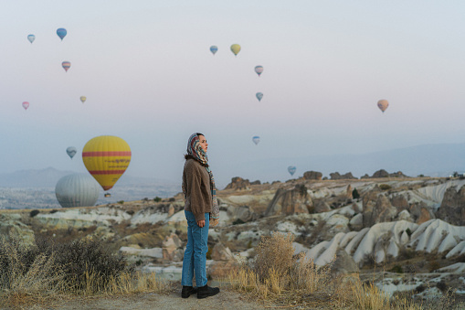Young Caucasian woman standing and looking at hot air balloons in  Cappadocia in Turkey